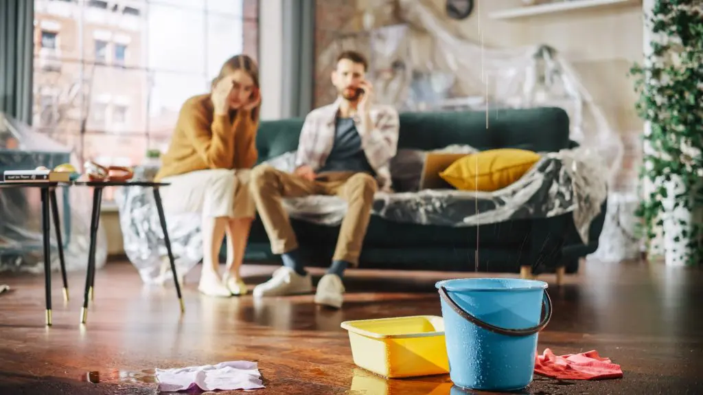 Roof is Leaking or Pipe Rupture at Home: Panicing Couple In Despair Sitting on a Sofa calling Insurers