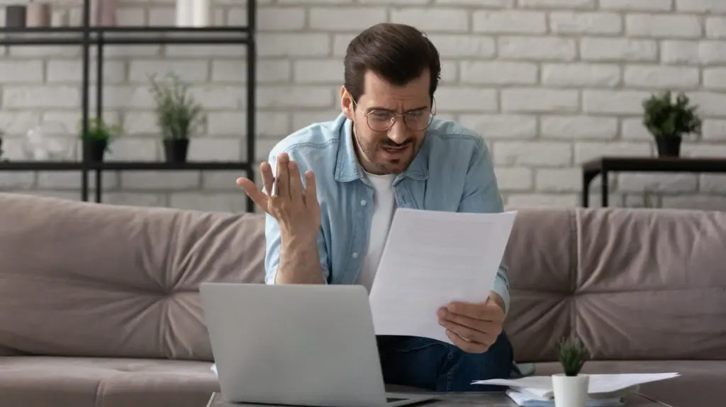 Annoyed young man sit on sofa work with home insurance papers