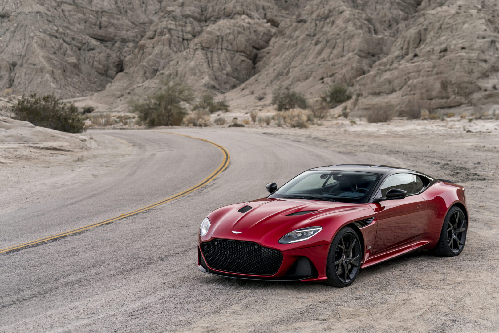 A new, red Aston Martin DBS Superleggera parked in the desert.