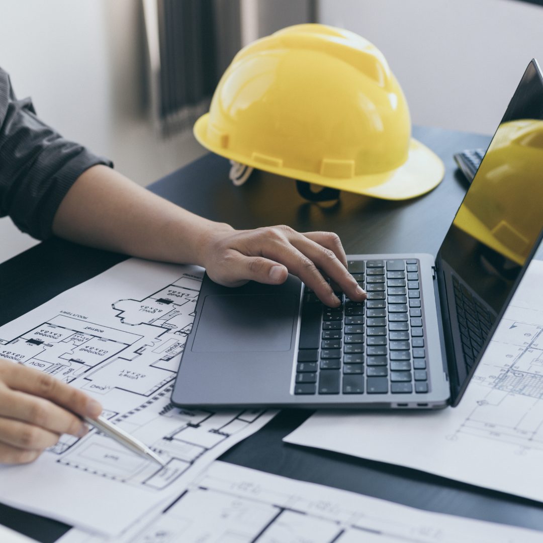 A close up of a laptop and hard hat in the background, in a professional office.